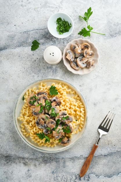 Pâtes fusilli aux champignons fromage et sauce crémeuse à l'ail sur assiette sur fond de table en pierre grise ou en béton Vue de dessus Cuisine italienne traditionnelle