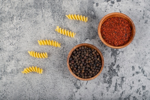 Pâtes fusilli crues avec diverses épices de poivre sur pierre.