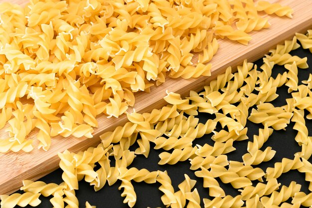 Pâtes fusilli non cuites éparpillées sur planche de bois