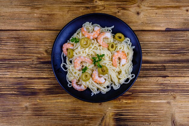 Pâtes italiennes aux crevettes et olives dans une assiette noire. Vue de dessus