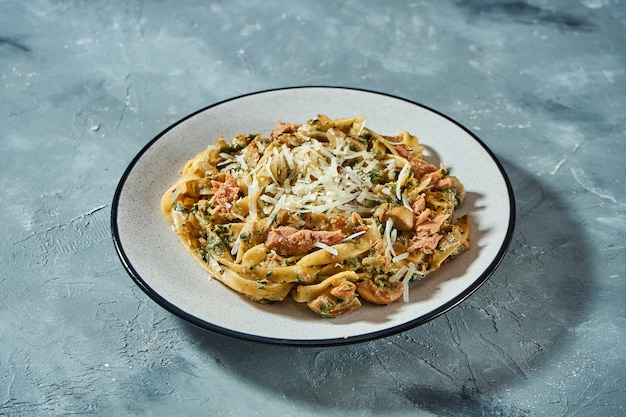 Pâtes italiennes aux fruits de mer, thon en conserve et parmesan dans une assiette grise sur fond gris. Gros plan, mise au point sélective