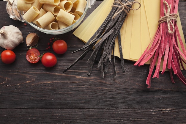 Pâtes italiennes colorées. Tagliatelles rouges et noires, feuilles de lasagne et ingrédients de cuisine sur fond de bois foncé, espace pour copie