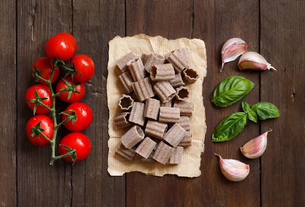 Pâtes italiennes crues, basilic et légumes sur table en bois