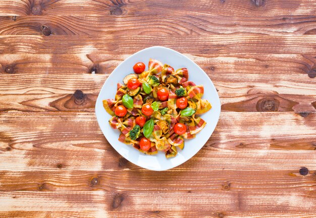 Pâtes italiennes farfalle à la sauce tomate et divers types de légumes sur un fond en bois