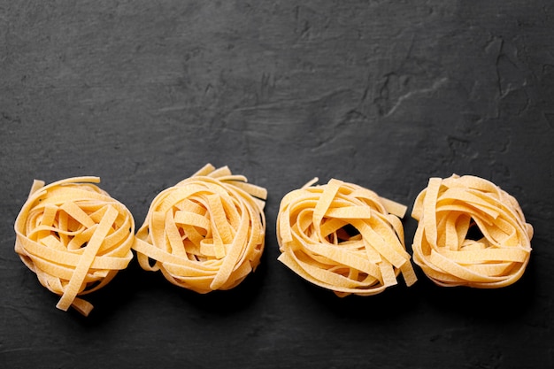 Pâtes italiennes fraîches l sur fond sombre avec espace de copie pour le texte. Nids de pâtes tagliatelles.