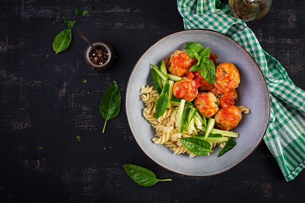 Pâtes italiennes. Fusilli aux boulettes de viande, concombre et basilic sur fond sombre. Dîner. Concept de restauration lente. Vue de dessus, mise à plat