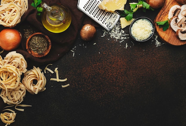 Pâtes italiennes non cuites champignons bruns champignons légumes fromage et ingrédients pour une cuisine savoureuse sur fond de table de cuisine ancienne vue de dessus de style sombre Bannière alimentaire