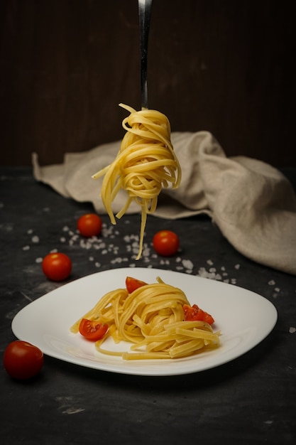 Pâtes italiennes sur une plaque sur un fond sombre avec des tomates cerises