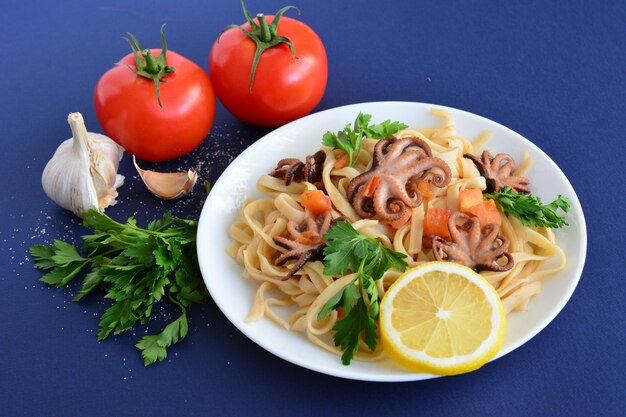 pâtes italiennes avec poulpe et tomates sur plaque blanche sur fond bleu