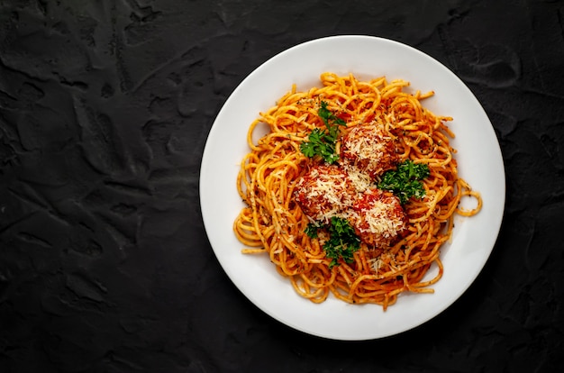 Pâtes italiennes avec sauce tomate et boulettes de viande dans une assiette avec des épices sur pierre