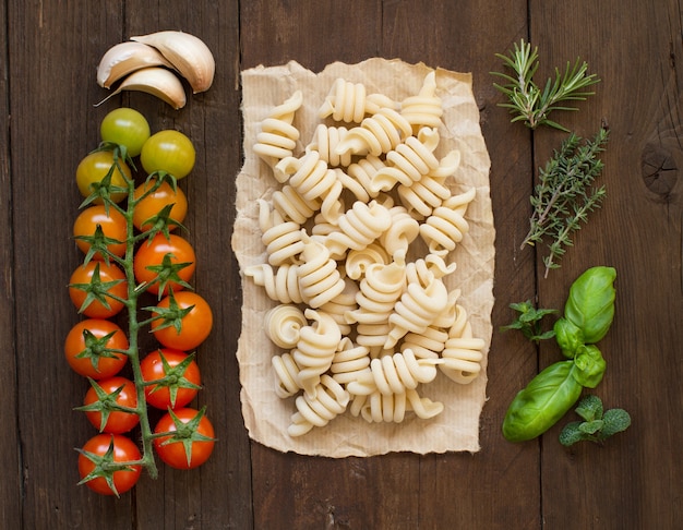 Pâtes italiennes, tomates et herbes sur une surface en bois