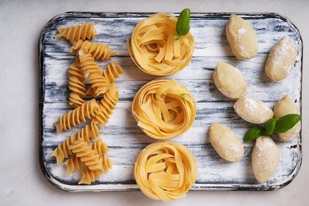 Pâtes italiennes traditionnelles: tagliatelles, fusilli et gnocchi décorés de feuilles de basilic. Concept de cuisine italienne. Vue de dessus. Mise à plat