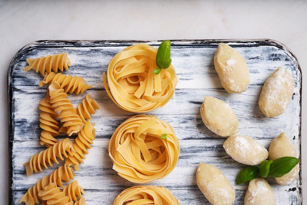 Pâtes italiennes traditionnelles: tagliatelles, fusilli et gnocchi décorés de feuilles de basilic. Concept de cuisine italienne. Vue de dessus. Mise à plat