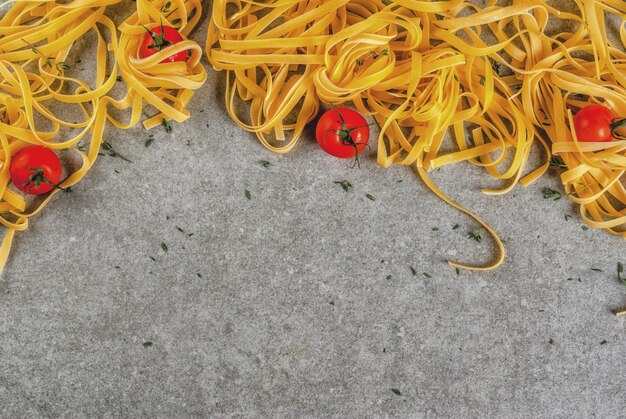 Pâtes italiennes traditionnelles Tagliatelles, sur table en pierre grise avec des ingrédients pour cuisiner le dîner - tomates, herbes, vue de dessus de fond