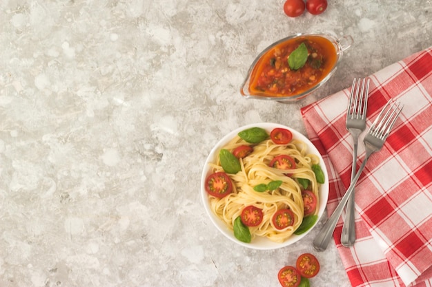 Pâtes marinara dans une assiette blanche sur une table blanche avec des quartiers de tomates et des feuilles de basilic.