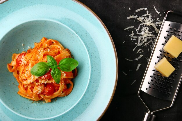 Pâtes marinara avec râpe à fromage et parmesan sur table sombre. Spaghetti à la sauce tomate et vue de dessus de basilic.