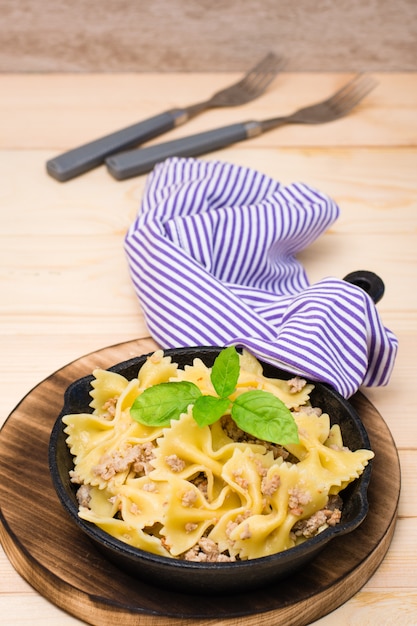 Pâtes marines prêtes à manger avec viande hachée et feuilles de basilic dans une poêle en fer sur une table en bois. Cuisine russe