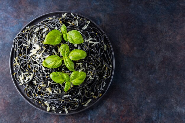 Pâtes noires au fromage râpé et basilic sur fond sombre