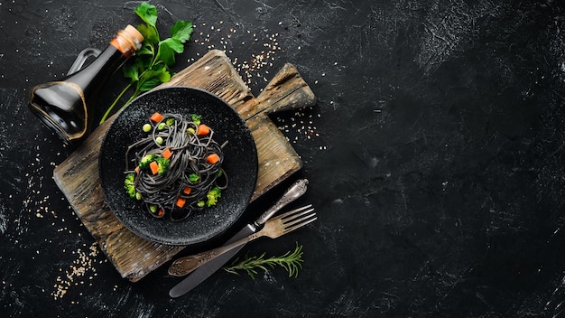 Pâtes noires aux légumes sur une plaque noire Vue de dessus Sur fond noir Espace de copie gratuit