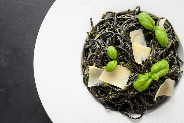 Pâtes noires encre de calmar spaghetti avec sauce pesto dans un bol noir sur fond noir.