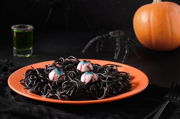 Pâtes noires italiennes d'Halloween décorées d'araignées amusantes dans une assiette orange sur fond noir