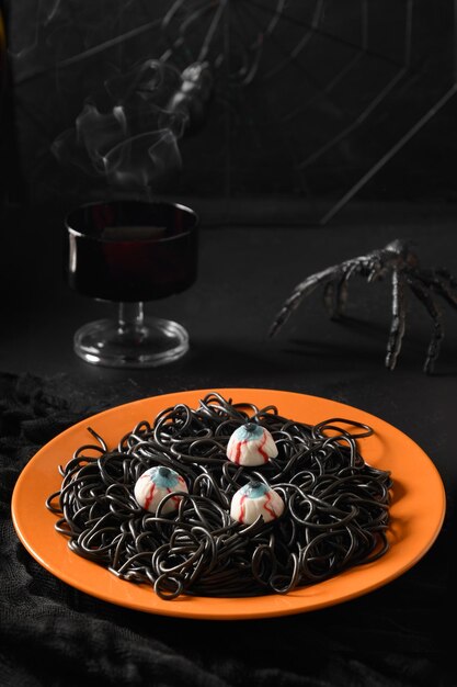 Photo pâtes noires italiennes d'halloween décorées d'araignées drôles dans une assiette orange sur blanc