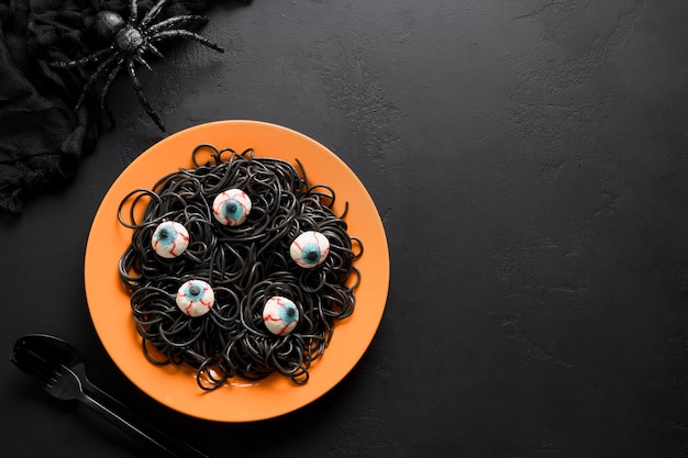 Pâtes noires italiennes d'Halloween décorées d'yeux d'horreur dans une assiette orange