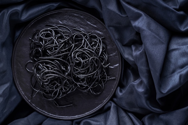 Pâtes noires sur une plaque noire. Pâtes noires à l'encre de seiche sur fond sombre. Spaghetti noir à l'encre de seiche. Espace de copie. Vue de dessus