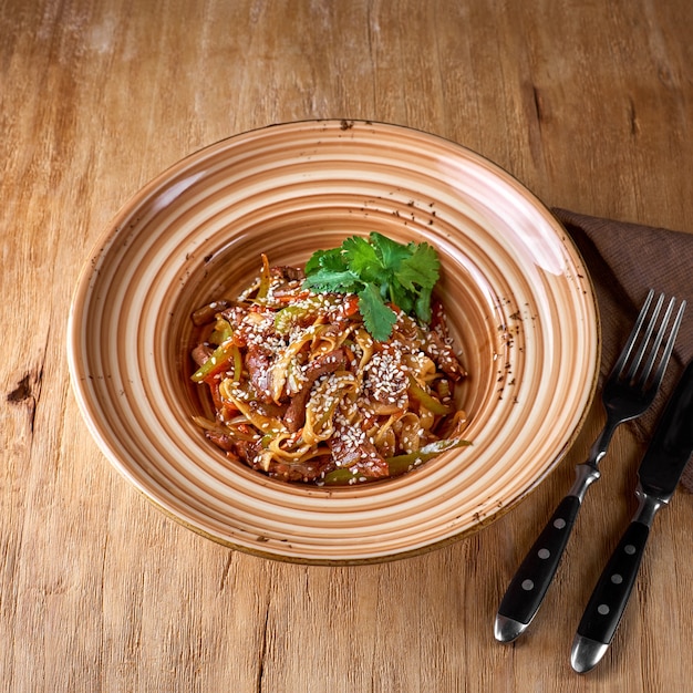 Pâtes nouilles udon- avec du bœuf et des légumes sur une assiette Sur une surface en bois.