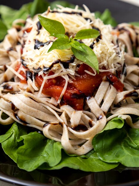 Pâtes de pâtes complètes au parmesan, feuilles vertes de roquette, sauce rouge et vinaigre balsamique sur plaque noire et fond de marbre blanc