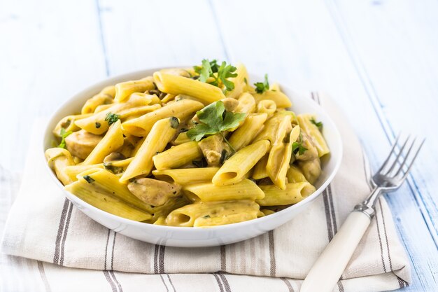 Pâtes pene avec morceaux de poulet champignons sauce parmesan et décoration aux herbes