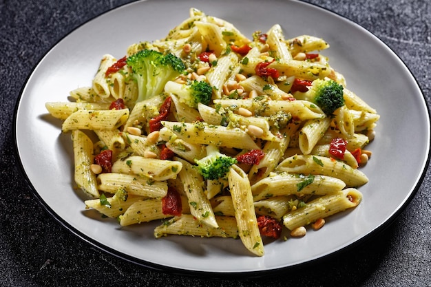 Pâtes penne au pesto de brocoli avec tomates séchées et pignons de pin sur une assiette, vue horizontale d'en haut, cuisine italienne, gros plan