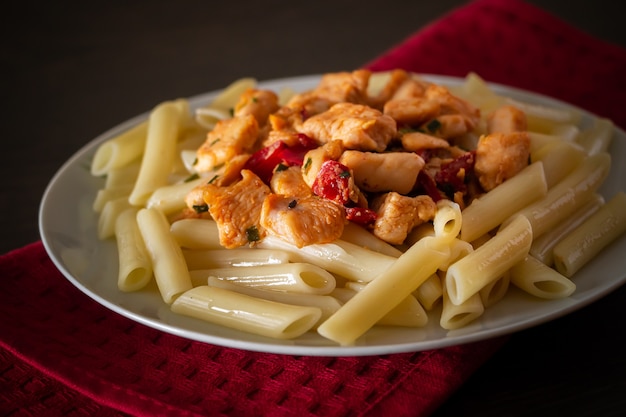 Pâtes penne au poulet et légumes à la sauce tomate. Délicieuses pâtes penne avec du poulet frit juteux sur une assiette sur une serviette rouge, fond sombre