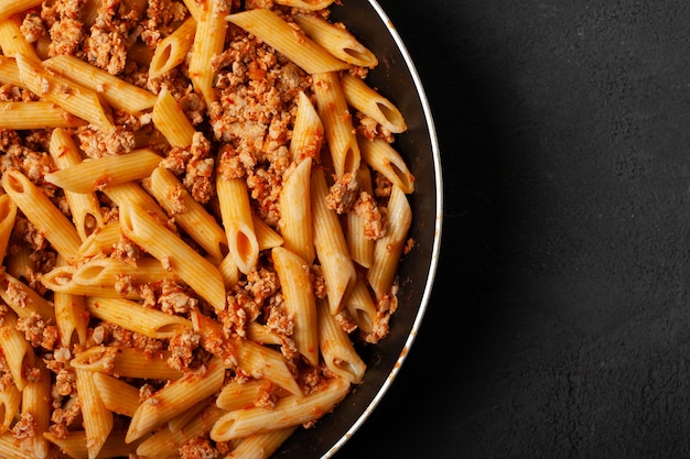 Pâtes penne italienne fraîche bolognaise sur poêle et fond en béton foncé vue de dessus avec copie espace.