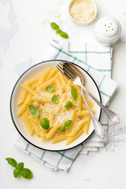 Pâtes penne rigate au parmesan et feuilles de basilic dans un plat en céramique sur une vieille table en béton léger.