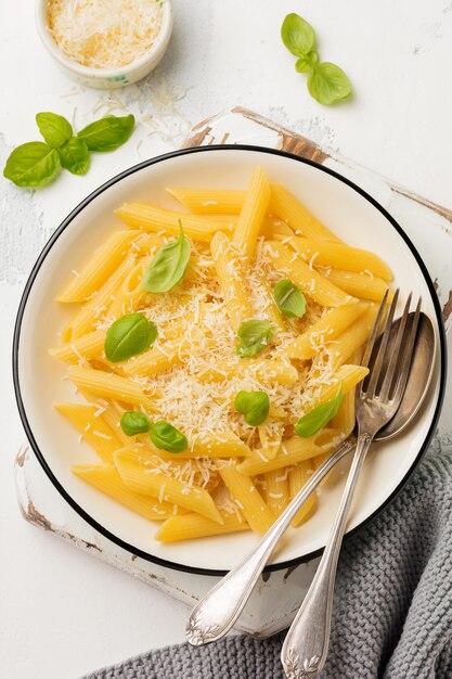 Pâtes penne rigate au parmesan et feuilles de basilic dans un plat en céramique sur une vieille table en béton léger.