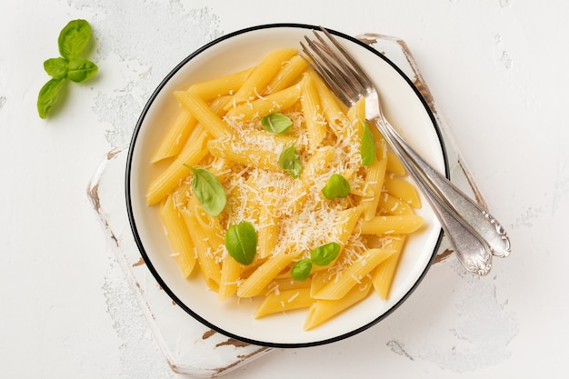 Pâtes penne rigate au parmesan et feuilles de basilic dans un plat en céramique sur une vieille table en béton léger.