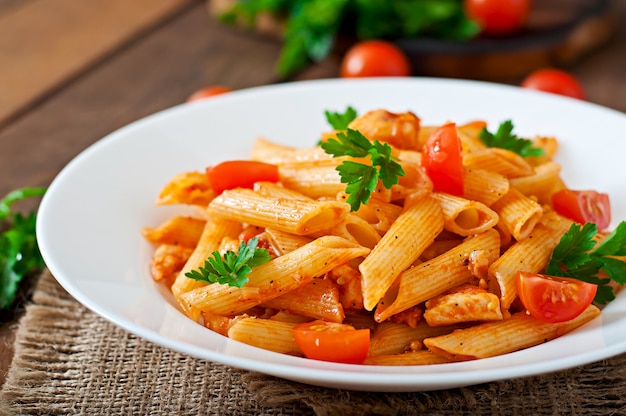 Pâtes penne à la sauce tomate au poulet et tomates sur une table en bois