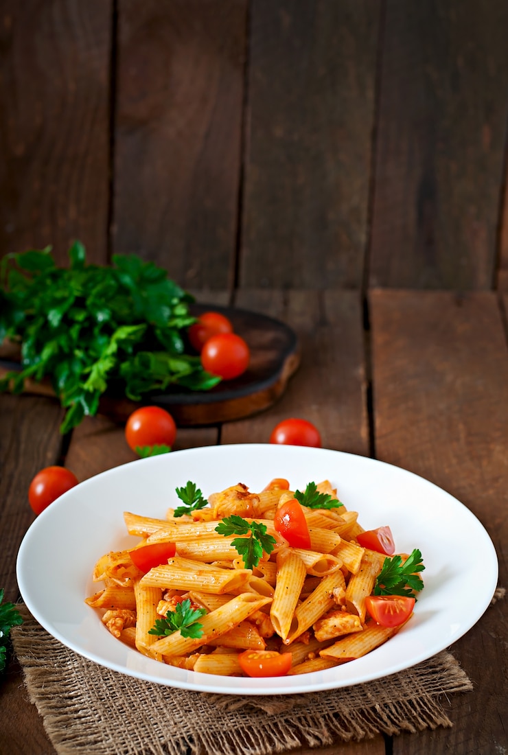 Photo pâtes penne à la sauce tomate au poulet et tomates sur une table en bois