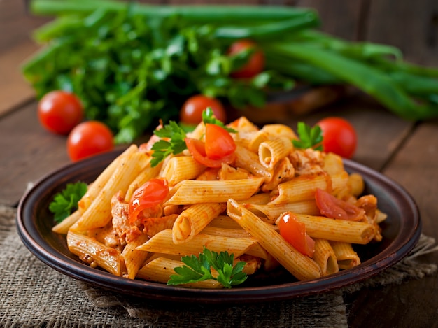 Pâtes penne à la sauce tomate au poulet et tomates sur une table en bois