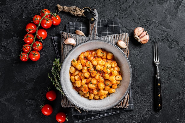 Pâtes de pommes de terre gnocchi avec sauce tomate et thym. Fond noir. Vue de dessus.