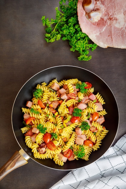 Pâtes Rotini aux pois verts, jambon et persil dans la poêle. Cuisine italienne.