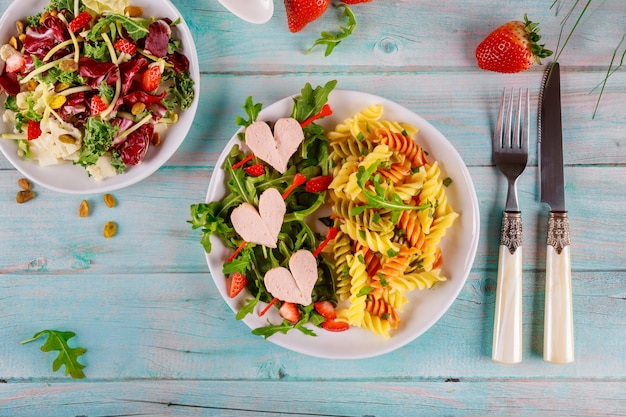 Pâtes rotini colorées, tomates cerises, coeurs de hot-dogs et salade. Concept de la Saint-Valentin.