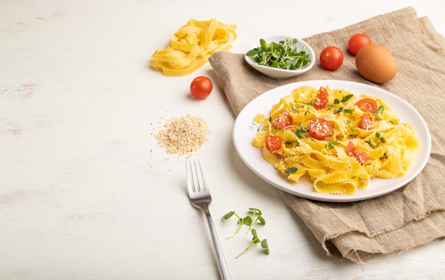 Pâtes à la semoule Reginelle à la tomate, aux œufs, au sésame et aux germes micro-verts sur un fond en bois blanc. Vue de côté,