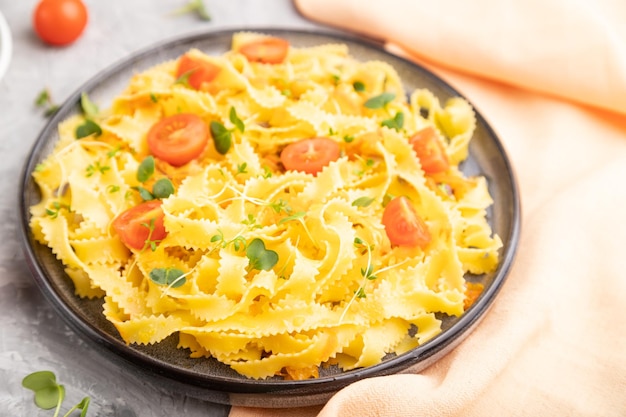 Pâtes de semoule Reginelle à la tomate, œufs et pousses micro-vertes sur fond béton gris et textile orange. Vue latérale, gros plan, mise au point sélective.