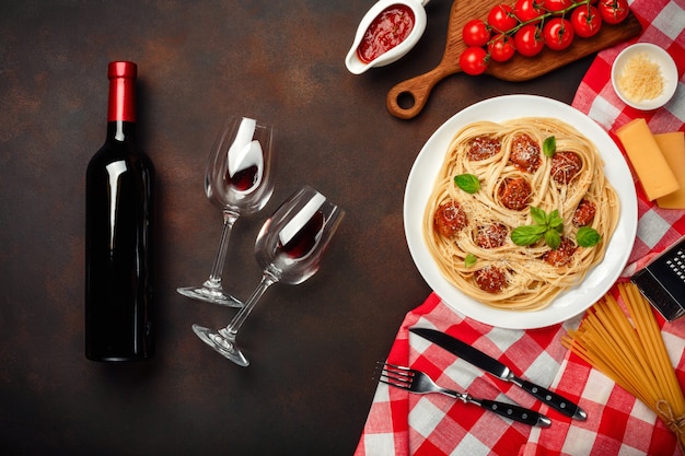 Pâtes spaghetti aux boulettes de viande, sauce tomate cerise, fromage, verre à vin et bouteille sur fond rouillé.