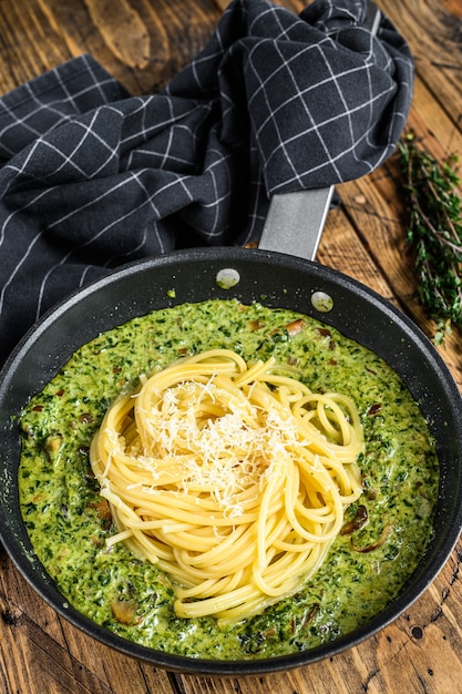 Pâtes spaghetti aux épinards dans une sauce à la crème avec du parmesan dans une poêle. Fond en bois. Vue de dessus.