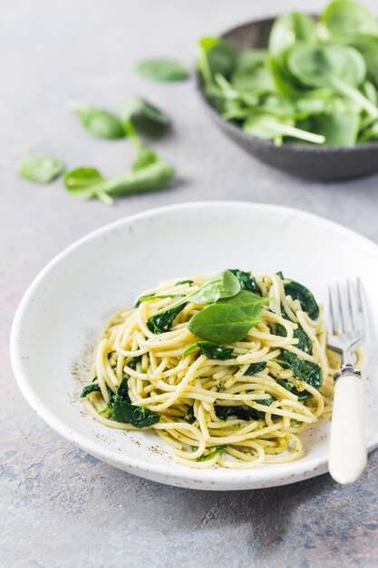 Pâtes spaghetti aux épinards et pesto vert, dans une assiette blanche sur fond de pierre grise