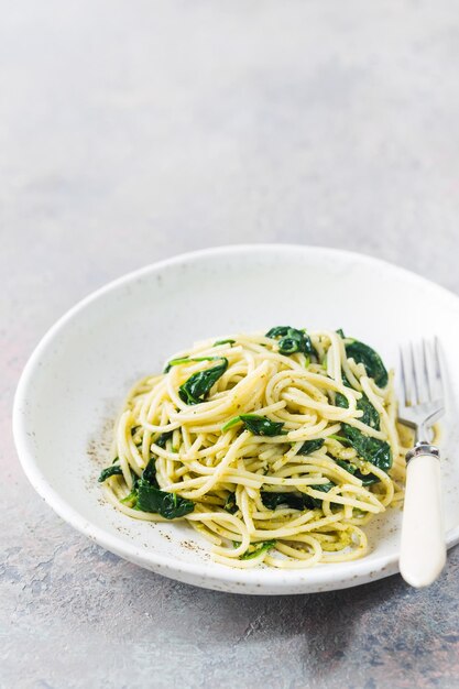 Pâtes spaghetti aux épinards et pesto vert, dans une assiette blanche sur fond de pierre grise