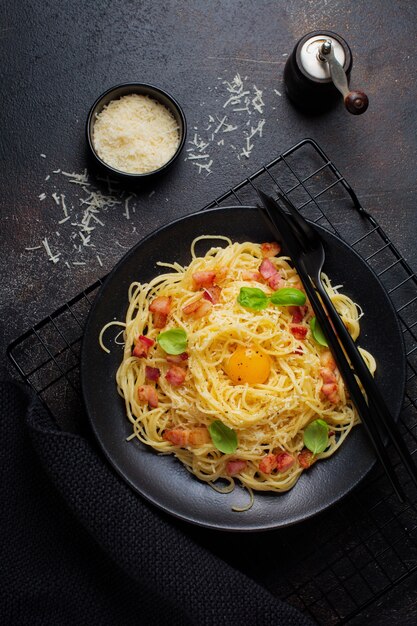 Pâtes spaghetti carbonara avec bacon, parmesan, jaune d'oeuf et feuilles de basilic sur une surface noire. Plat italien traditionnel